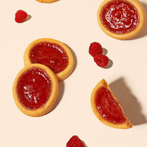 Crunchy Raspberry Cookie Tarts and fresh raspberries on a pink background